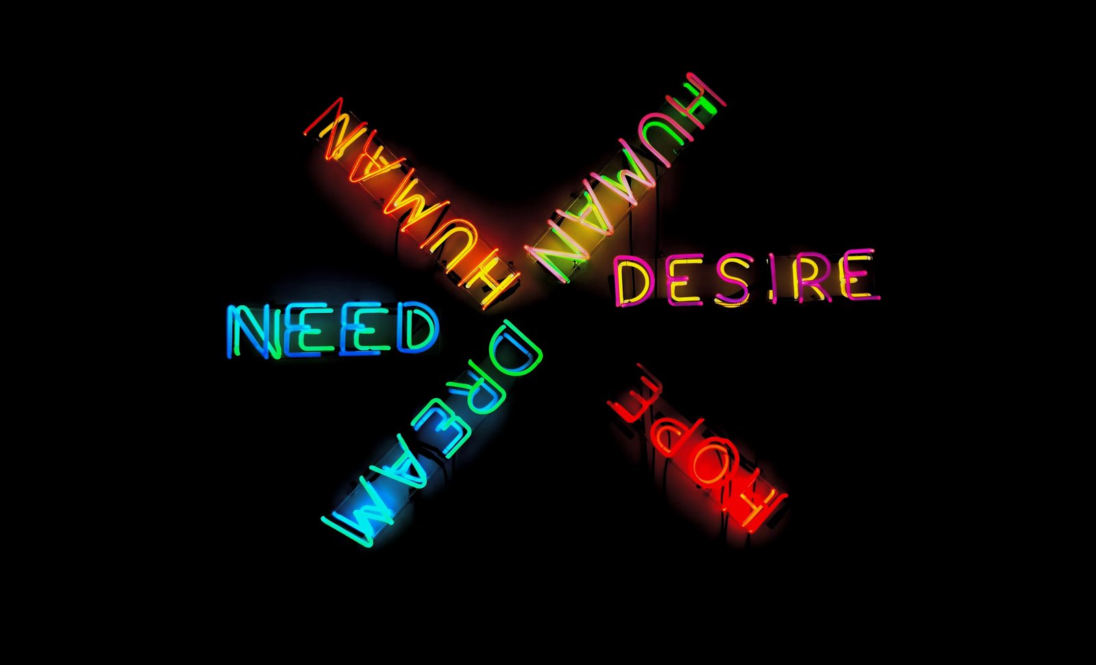 Neon signs reading NEED, DESIRE, HOPE, DREAM, HUMAN radiating outward