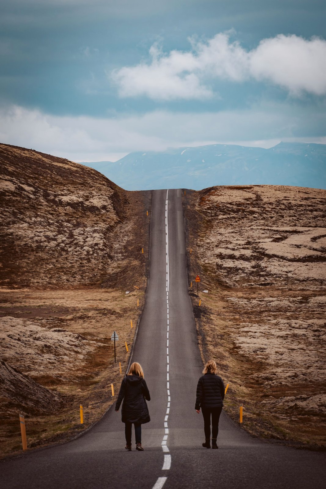 Two people walking a long open road toward distant hills